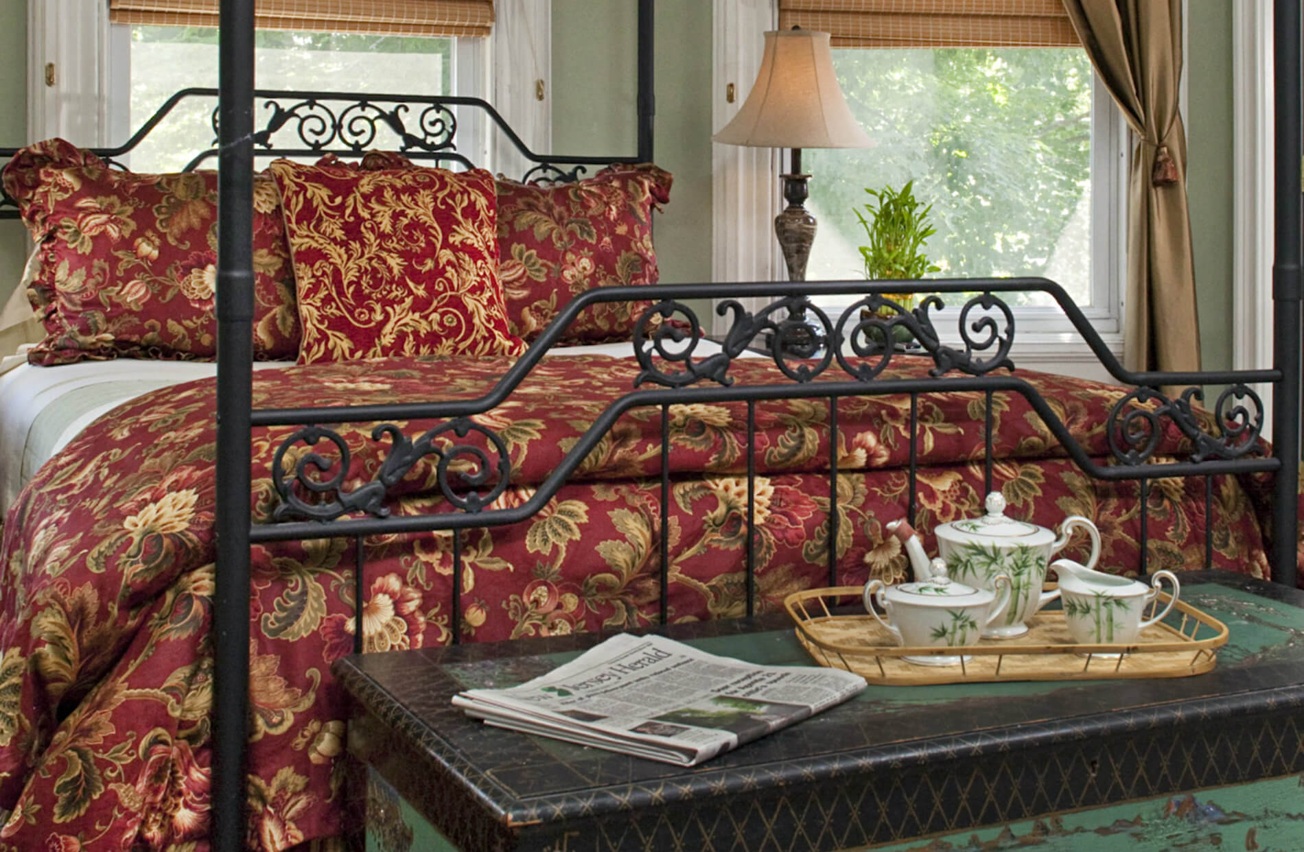 Iron bed with red and gold bedding and seat at foot of bed