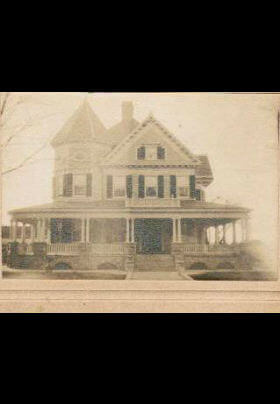 Old sepia photo of large house with large front porch and gabled roof