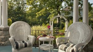 two white wicker chairs, a white wicker table, ice tea and a flower in a bud vase.