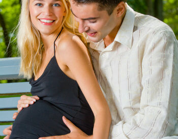 Pregnant blonde woman embraced by dark-haired man