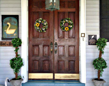 Large wooden doors with green topiaries on either side and gold kickplates