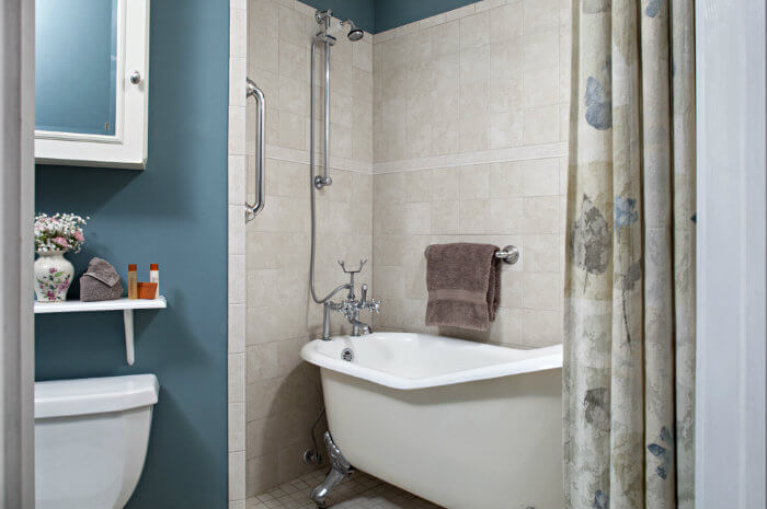 White claw-foot tub in tile surround with flowered shower curtain