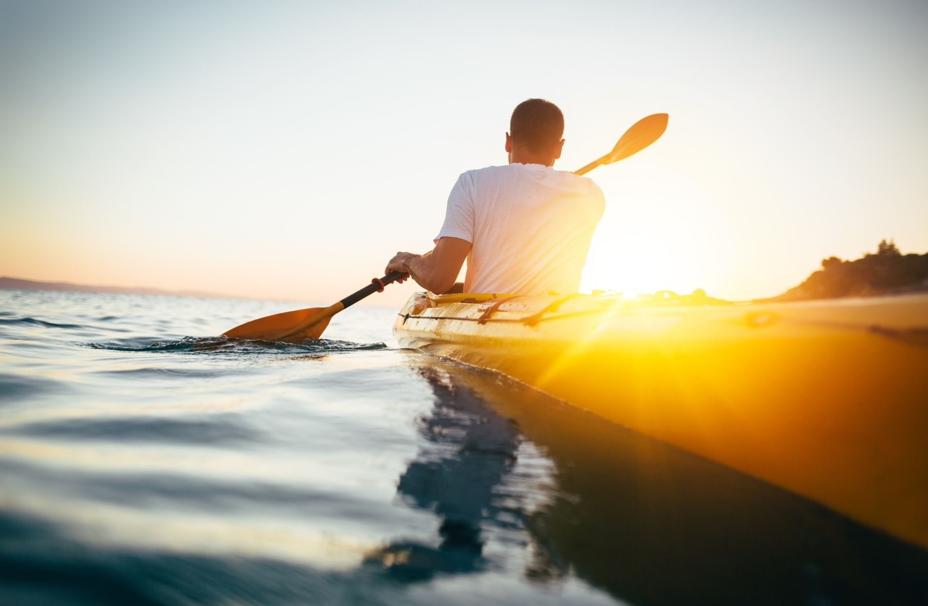 Man in white t-shirt paddling a yellow kayak as the sun sets